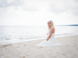 en gravid blivande mamma sitter i den mjuka sanden på den magiska stranden och håller på sin gravidmage