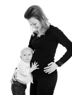 ett porträtt på en gravid mamma mot vit stilren bakgrund där hennes son håller på magen och lyssnar