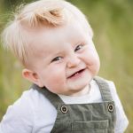 en 1-årig pojke ler mot kameran och hans små nya tänder syns