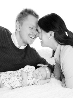 nyblivna föräldrar ler mot varandra och deras baby ligger och sover i deras famn