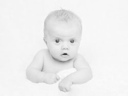 nyfödd baby kikar nyfiket i kameran liggandes på en vit stilren och mysig filt