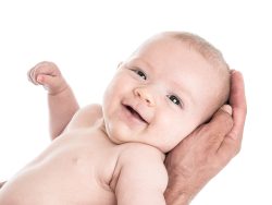en nyfödd bebis ligger i pappans händer och ler