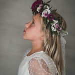 en flicka med blomsterkrans och vacker spetstopp mot en mjukt belyst grå bakgrund