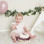 ettårig flicka äter tårta i en mysig studiokuliss under en smash the cake fotografering